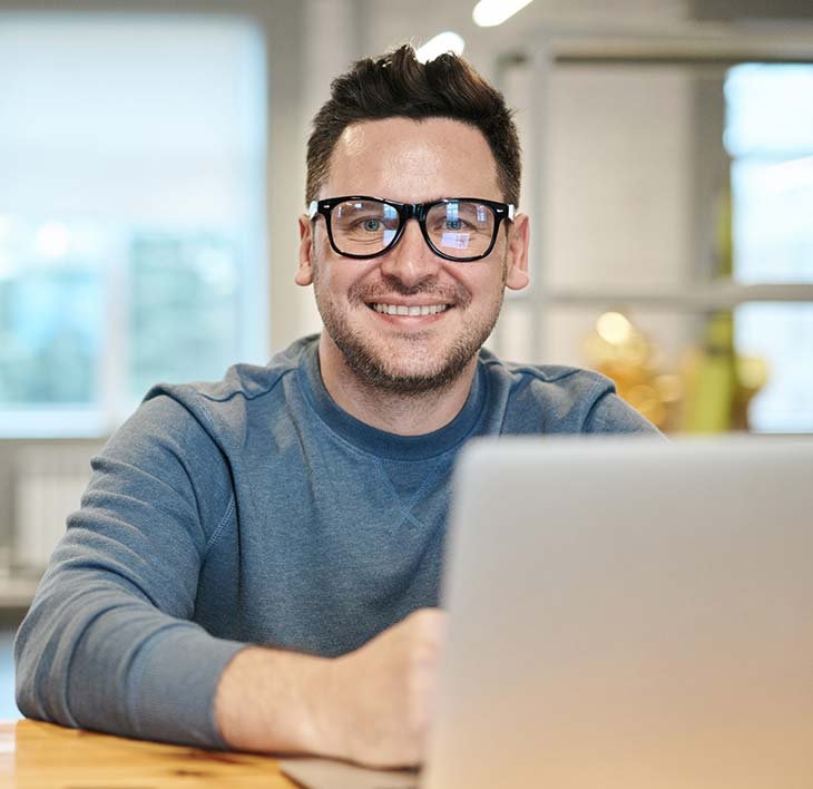 Man with Glasses Smiling Behind Laptop Man with Glasses Smiling Behind Laptop